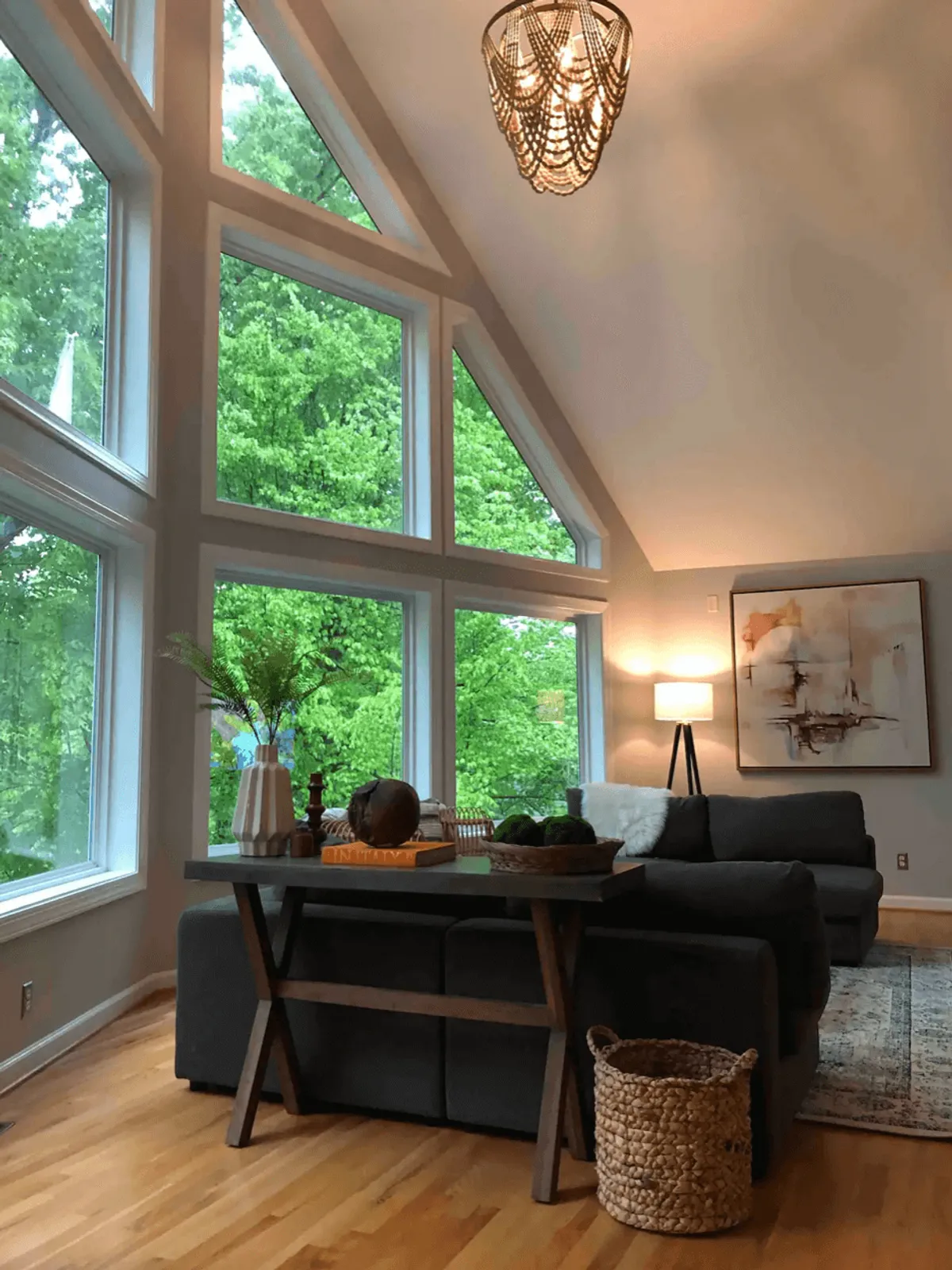 A spacious living area featuring large floor-to-ceiling windows that flood the room with natural light and showcase breathtaking lake views. The modern sofa, decorative artwork, and cozy wooden table with stylish accents invite relaxation and socializing in a tranquil setting.