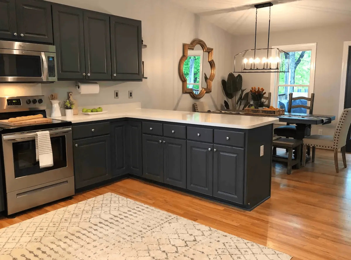 This image features a stylish, modern kitchen with a prominent island, sleek stainless steel appliances, and a spacious dining table nearby. Decorative touches, like a well-placed mirror, enhance the inviting atmosphere, while the setup clearly supports cooking and entertaining. The visible layout suggests easy flow between kitchen prep and communal dining.