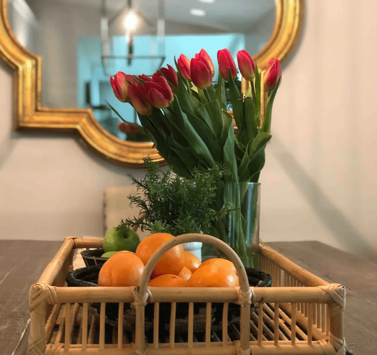 A bright and cheerful room with a vase of tulips as the centerpiece, a basket of fresh fruits, and a decorative mirror suggesting a welcoming gathering space. The setup hints at social interactions and a relaxed environment for group activities.